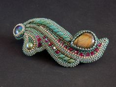 a brooch that is sitting on a black surface with beads and stones around it