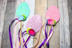 three paper flowers with ribbons around them sitting on a wooden floor next to each other