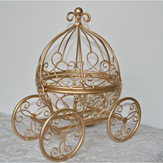 a golden metal carriage with wheels on a white tableclothed surface, in the shape of a birdcage