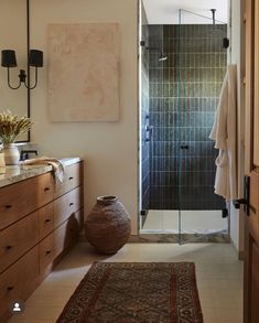 a bathroom that has a rug on the floor and a vase with flowers in it