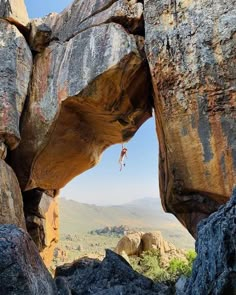 a man hanging from the side of a large rock formation with mountains in the background