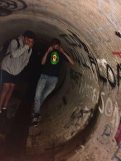 two people standing in a tunnel with graffiti on the walls and one person holding a green frisbee