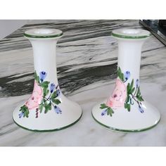 two white vases with pink and blue flowers on them sitting on a marble table