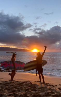 two women holding surfboards on the beach at sunset