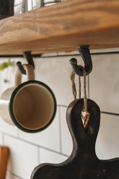 two coffee mugs hanging from hooks on a kitchen wall with white tiles and wooden shelves