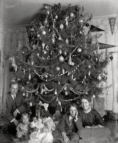 an old black and white photo of a family sitting in front of a christmas tree