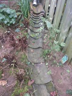 a person standing on top of a stone walkway next to a wooden fence and green plants