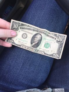 a person is holding a ten dollar bill in their lap