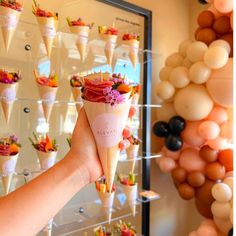 a person holding up an ice cream cone with flowers on it in front of balloons