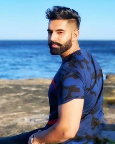 a man with a beard sitting on rocks near the ocean