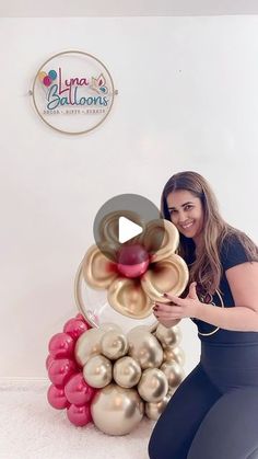 a woman kneeling down next to a bunch of balloons in front of a white wall