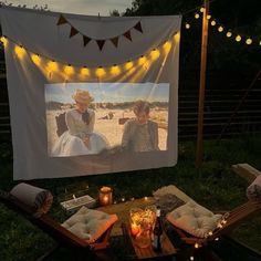 an outdoor movie screen with two people sitting in chairs and candles on the ground next to it