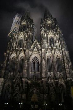 the large cathedral is lit up at night with dark clouds in the sky behind it