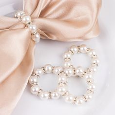 two bracelets with pearls are on a plate next to a pink satin bow tie