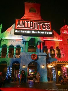 an illuminated mexican food restaurant at night with people standing outside the building and lights on