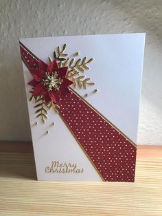 a christmas card with a red ribbon and poinsettis on the front, sitting on a table