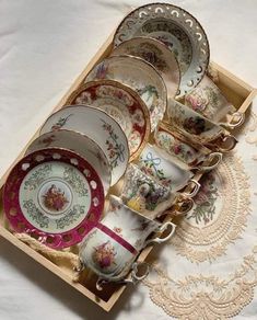 an assortment of china dishes in a wooden box on a table with lace doily