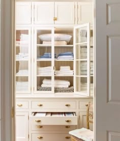 an open closet with white linens and folded towels in it's glass doors