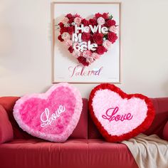 two heart shaped pillows sitting on top of a red couch next to a framed poster