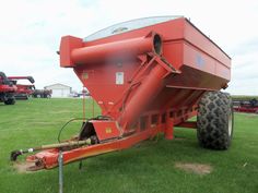 a red tractor trailer sitting on top of a lush green field next to other farm equipment