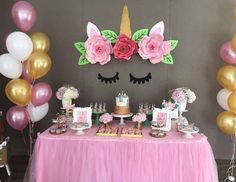 a table topped with lots of pink and gold balloons next to a unicorn face cake