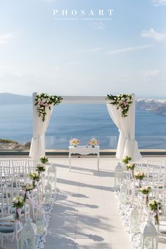 an outdoor ceremony setup with white chairs and flowers on the aisle, overlooking the ocean