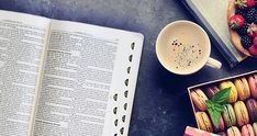 an open book next to a cup of coffee and macaroons