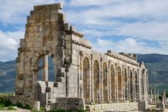 an old stone building with columns and arches in front of a mountain range behind it