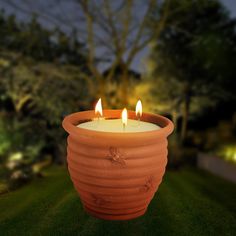 two lit candles in a clay pot on the grass