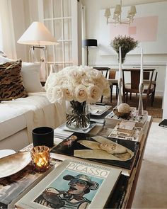 a living room filled with furniture and flowers on top of a coffee table in front of a window