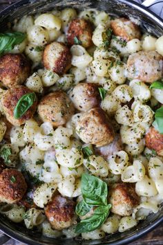 a skillet filled with pasta and meatballs covered in cheese, herbs and seasoning