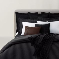 a bed with black and white sheets, pillows and blankets on it's headboard