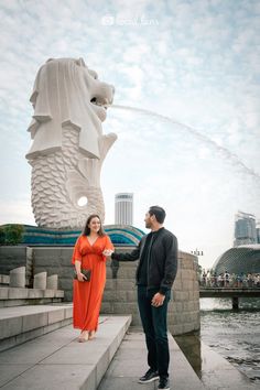 a man standing next to a woman in front of a water fountain with a lion statue