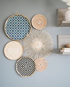 several woven baskets hanging on the wall above a vase with flowers and books in it