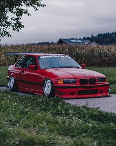 a red car parked on the side of a road next to a tree and cornfield