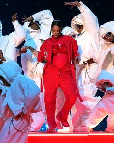 a woman in red jumpsuits standing on stage with other dancers behind her, all dressed in white