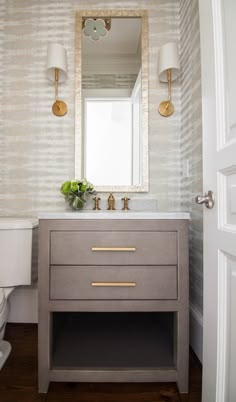 a white toilet sitting next to a bathroom sink under a mirror on top of a wooden floor