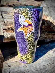 a purple and yellow tumbler sitting on top of a piece of wood