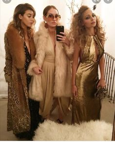 three beautiful women standing next to each other in front of a white wall holding a cell phone