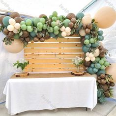 a table topped with balloons and greenery next to a wooden bench