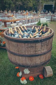 a wooden barrel filled with lots of bottles on top of a lush green field next to tables