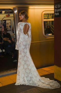 a woman in a white dress standing on a subway platform with her back to the camera