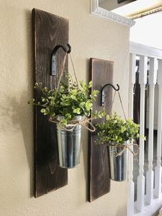 two metal buckets with plants hanging from them on a wall next to a banister