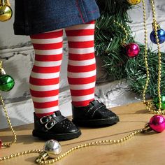 a child's legs in striped stockings and black shoes with christmas decorations on the floor