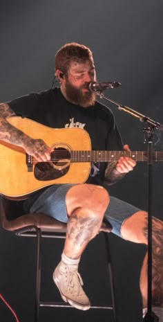 a man sitting in a chair with a guitar on his lap and microphone to his side