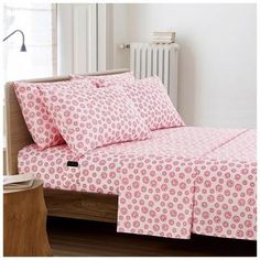 a bed with pink bedspread and pillows in front of a radiator