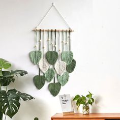 a wall hanging with green leaves on it next to a wooden table and potted plant