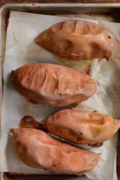 three baked sweet potatoes sitting on top of a baking sheet with wax paper around them