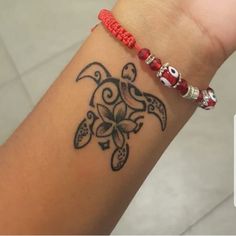 a woman's arm with a turtle tattoo on it and a red beaded bracelet