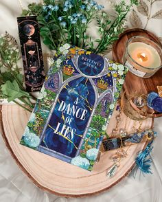 a book sitting on top of a table next to a candle and some flowers in front of it